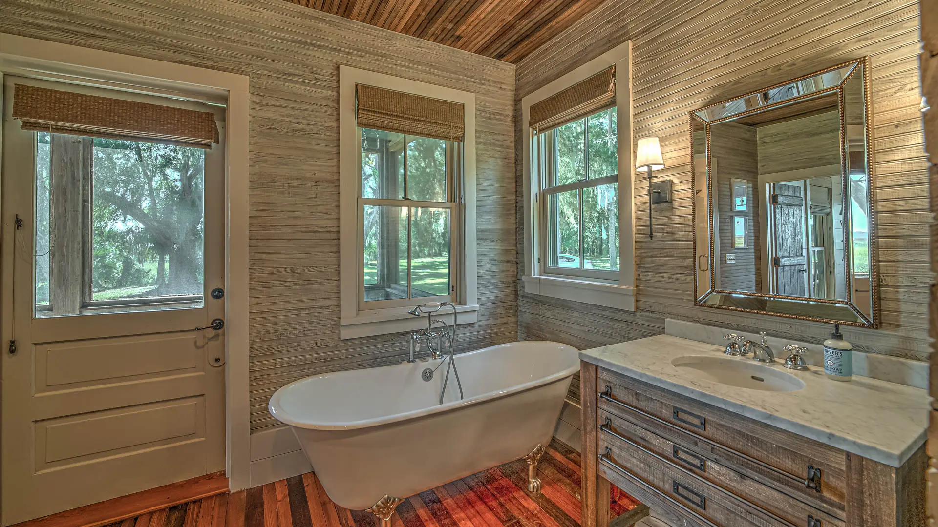 A rustic bathroom featuring a white clawfoot bathtub, a wooden vanity with a white countertop, and textured walls under a wooden plank ceiling.