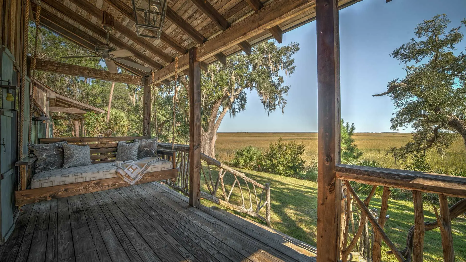A rustic wooden porch with a cozy daybed overlooking a scenic landscape of golden fields and mossy trees.