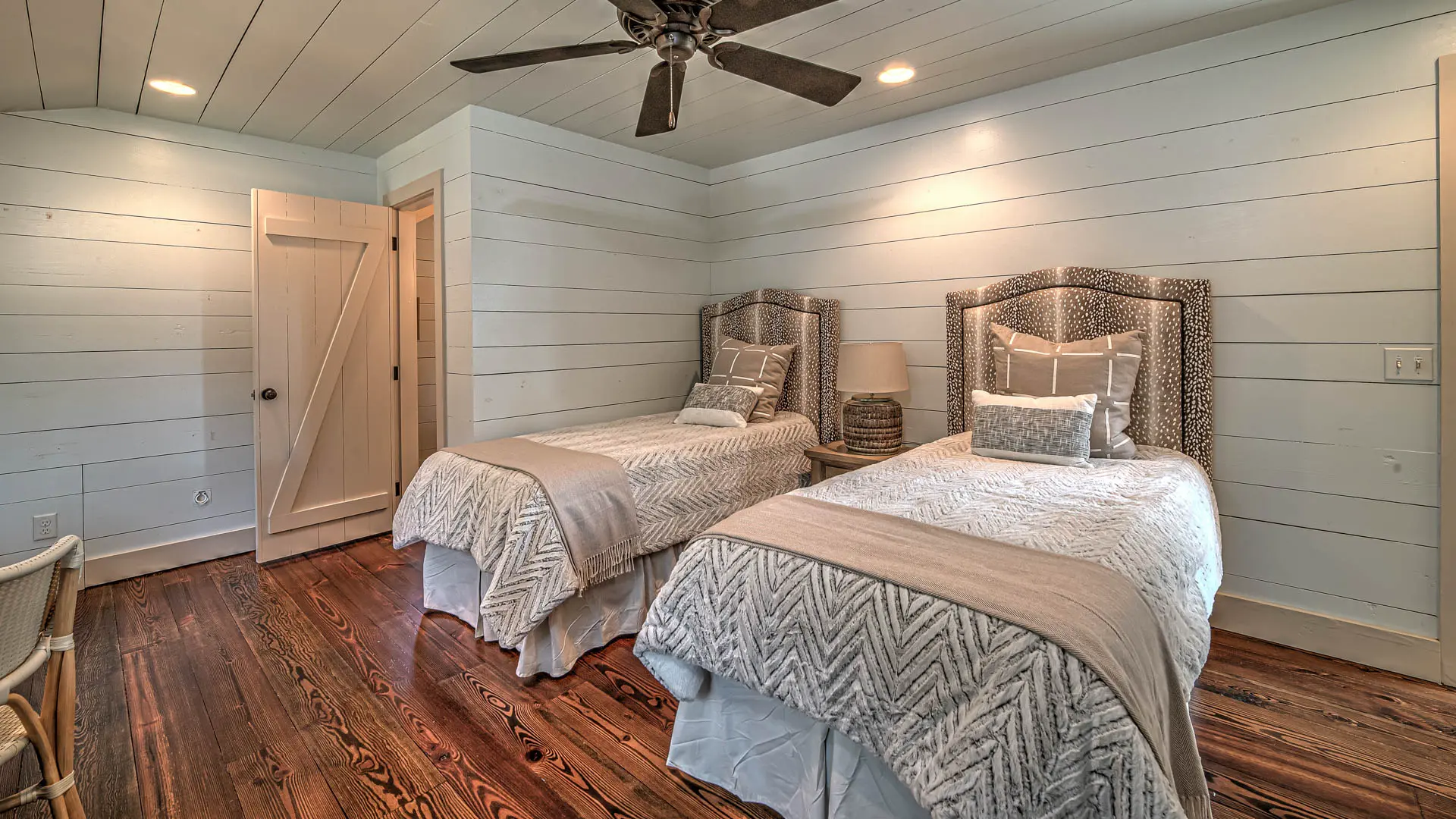 A cozy bedroom with two twin beds featuring matching patterned bedding and headboards, set against light blue shiplap walls and dark hardwood floors.
